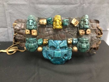 M.T.O., Dk Brown, Turmeric Yellow, Turquoise Blue, Gold, Leather, Fiberglass, Mayan Influenced Belt. Reptile Textured Brown Leather with Turquoise & Turmeric Skulls & Mayan God Headpieces Sculpted In Fiberglass/resin with Gold Painted Beads, Leather Wang Lacing At Center Back, Waist